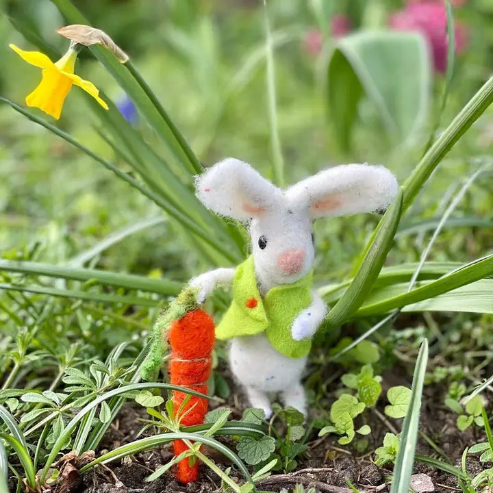 Felted white bunny with carrot in front of a daffodil 